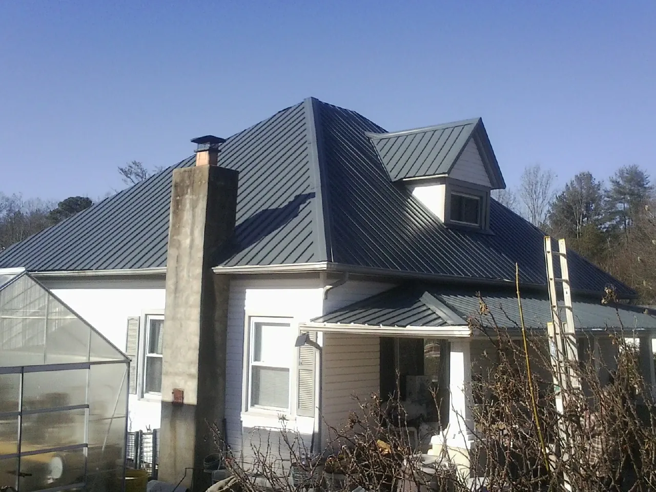 Dark blue standing seam metal roof on a white farmhouse with dormer — Slate & Tile Roof Repair by Roofing Brothers in Byrdstown