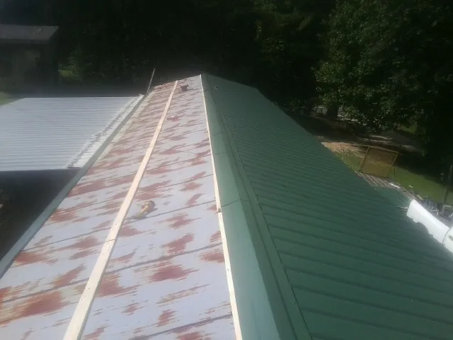 Old rusted panels beside newly installed green metal roofing — Wind Damage Roof Repair by Roofing Brothers in Byrdstown