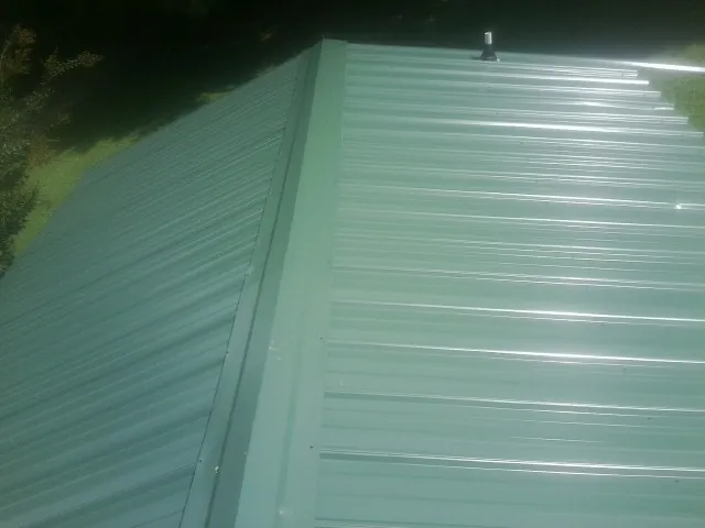 New green metal panels meeting at the ridge of a roof — Flat Roof Repair work by our crew in Byrdstown