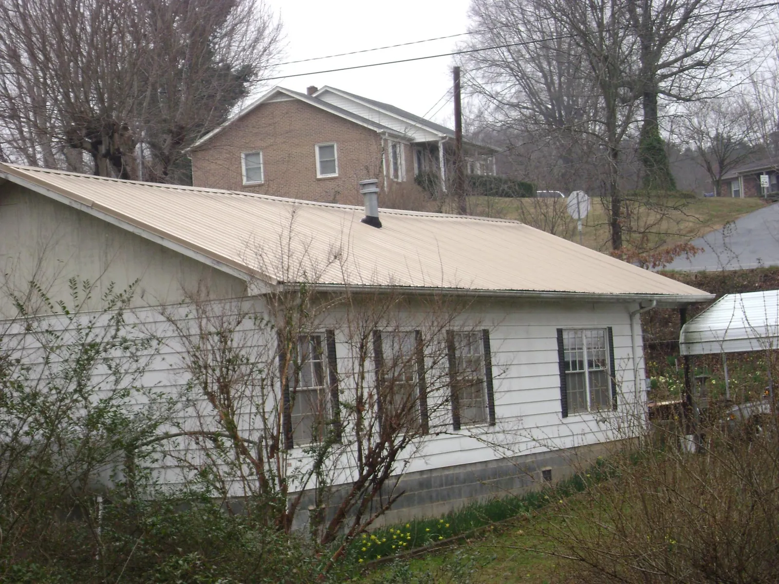 Tan metal roof on a white sided house set into a hillside — Commercial Roofing by Roofing Brothers in Byrdstown