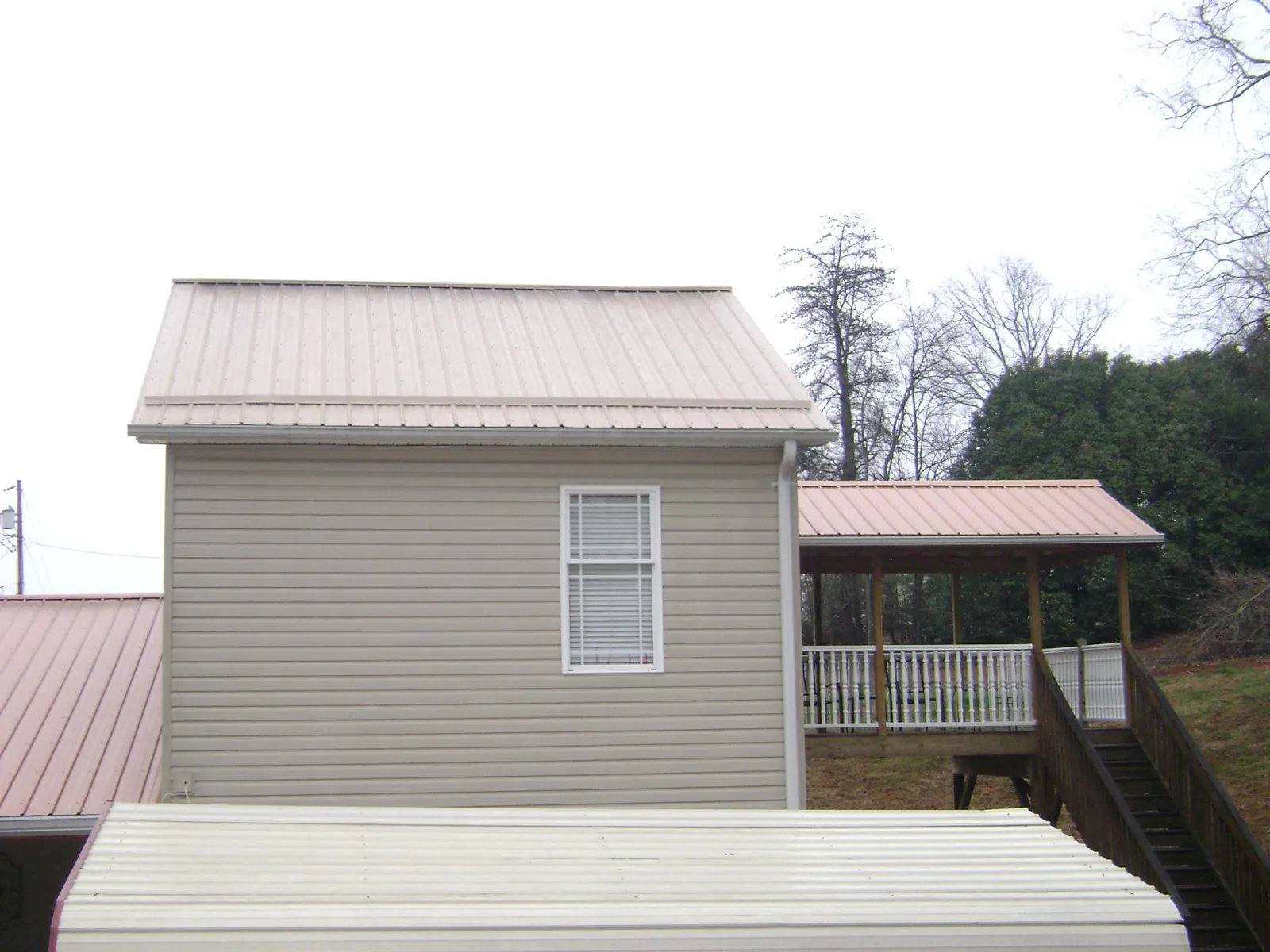 Tan metal roofs on a two story addition and attached porch, from a Roof Replacement job in Byrdstown